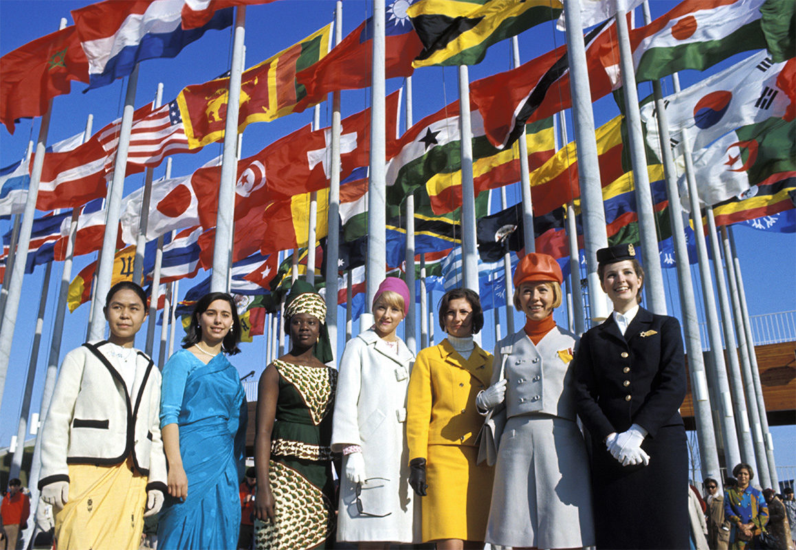 Hôtesses devant les drapeaux à la Place des Nations © Gouvernement du Canada. Reproduit avec la permission de Bibliothèque et Archives Canada (2016). Source : Bibliothèque et Archives Canada/Fonds de la Compagnie canadienne de l'exposition universelle de 1967/e000990933