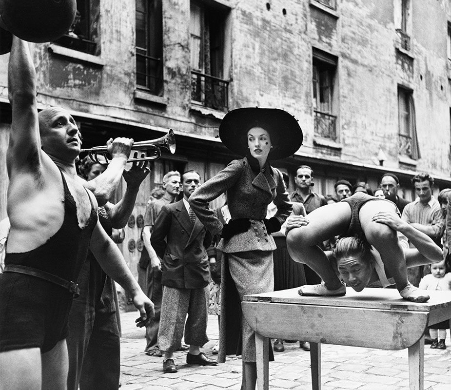 Elise Daniels with street performers, suit by Balenciaga, Le Marais, Paris, 1948. Photograph by Richard Avedon © The Richard Avedon Foundation